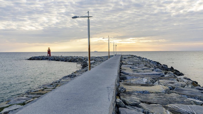 Sonnenaufgang mit Leuchtturm an einer Hafenmole.