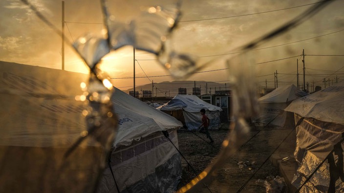 Ein zerschossene Scheibe, dahinter das Flüchtlingscamp Badarash im Nordirak.