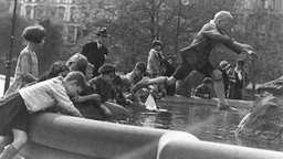 Eine Gruppe von Kindern spielt 1930 an einem Brunnen, schwarz-weiß Bild.