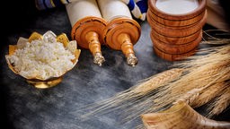 Traditionelle Milchspeisen und Getreide liegen neben einer Torarolle auf einem Tisch