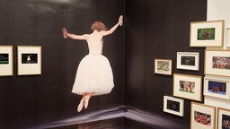 Ausstellungsansicht: Darstellung einer Balletttänzerin, die zwischen gerahmten Bildern aus Fußballspielen schwebt.