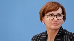 Bundesministerin für Bildung und Forschung Bettina Stark-Watzinger im Halbseiten-Profil vor einem blauen Hintergrund.