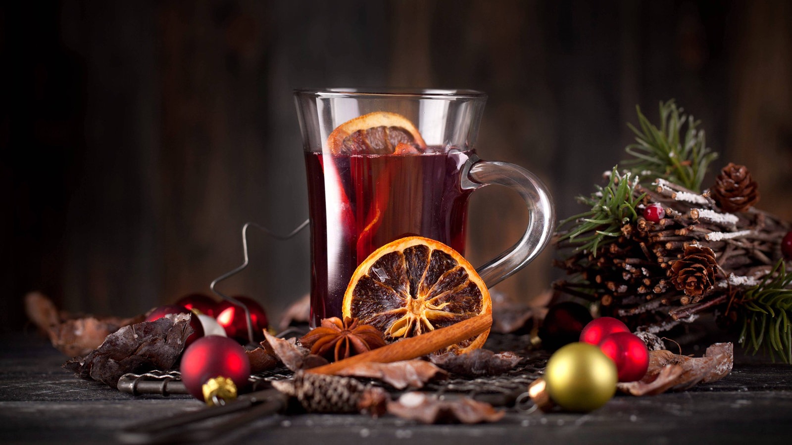 Ein Glas mit Punsch umrandet von Gewürzen und weihnachtlicher Dekoration.