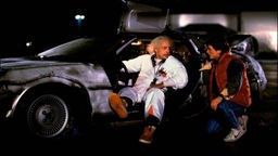 Filmszene aus "Zurück in die Zukunft" (1985): Michael J. Fox und Christopher Lloyd vor ihrem DeLorean DMC-12