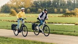 Eine Frau und ein Mann fahren auf einem E-Bike durch eine Wiesen-Landschaft