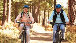 Ein älteres Paar ist mit Fahrrädern im Wald unterwegs