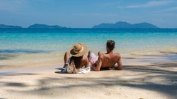 Eine Frau und ein Mann liegen am Strand mit Blick aufs Meer
