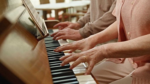 Ein Seniorenpaar spielt gemeinsam am Klavier.