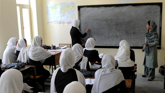15 Mädchen mit Kopftuch sitzen in einem Klassenzimmer und blicken auf die Tafel