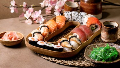 Neben einem Teller mit feinem Sushi steht ein Becher und eine kleine Schale mit Algensalat.