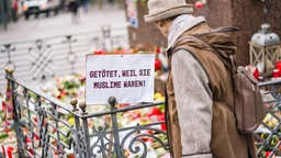 Eine Frau steht im Februar 2020 auf dem Marktplatz von Hanau, wo die Bürger mit Blumen, Plakaten und Kerzen ihre Trauer zum Ausdruck bringen. Auf einem Schild steht: "Getötet, weil sie Muslime waren!"