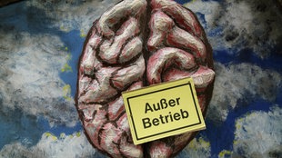 Gemaltes Bild eines Gehirns und ein Schild mit der Auschrift "Außer Betrieb"