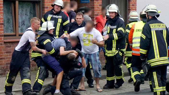 Drei Männer behindern bei einem Einsatz die Arbeit von Polizei und Feuerwehr und greifen dabei einen Polizisten körperlich an.