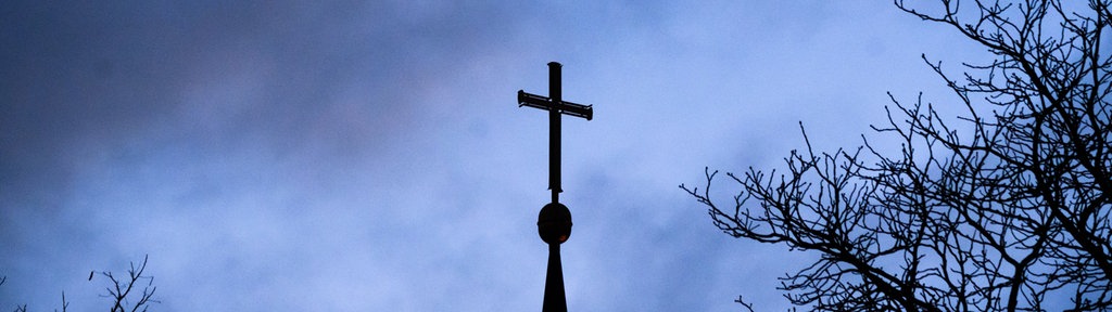 Dunkle Wolken ziehen über das Kreuz auf einer evangelischen Kirche in der Region Hannover hinweg