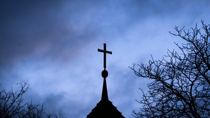 Dunkle Wolken ziehen über das Kreuz auf einer evangelischen Kirche in der Region Hannover hinweg