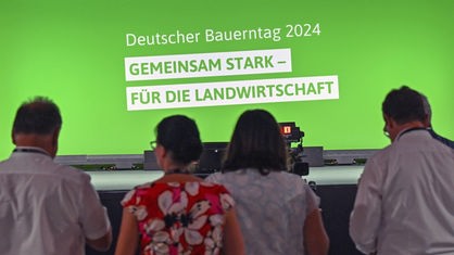 Teilnehmer:innen des Bauerntag Cottbus vor einer Bühne. Auf einer grünen Leinwand auf der Bühne steht "Deutscher Bauerntag 2024. Gemeinsam stark - für die Landwirtschaft"