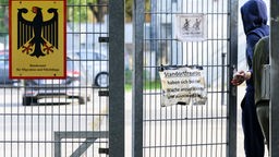 Geflüchteter im Kapuzenpullover geht durch die Tür in einem Gitterzaun der Landesaufnahmebehörde Braunschweig