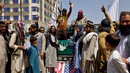 Mitglieder und Unterstützer der Taliban stehen auf einer US-Flagge, während sie am 14. August 2024 in Kabul, Afghanistan, eine Kundgebung zum dritten Jahrestag des Falls Kabuls abhalten.