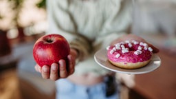 Ein Mensch hält einen Apfel und einen Donut in den Händen.