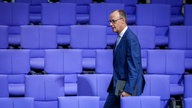 Friedrich Merz geht durch leere Sitzreihen des Bundestages