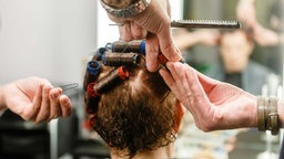 Ein Friseur wickelt die Haare einer Kundin auf Lockenwickler.