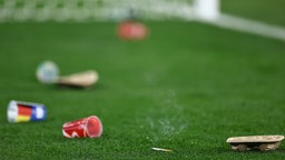 Auf dem leeren Rasen vor einem Tor liegt Abfall, den Stadionbesucher auf das Spielfeld geworfen haben