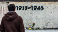 Rosen liegen am Boden vor einer Mauer des KZ Dachau auf der die Jahreszahlen "1933 - 1945" angebracht sind