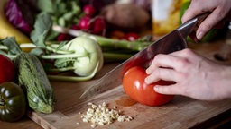 Eine Frau schneidet mit einem Messer eine Tomate auf einem Holzbrett klein. Symbolbild