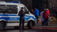 Menschen versammeln sich vor der Johanniskirche in Magdeburg. Davor sperrt ein Fahrzeug der Polizei die Straße.