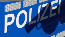 Schatten einer Waffe auf dem Schriftzug "POLIZEI" an der Tür eines Einsatzfahrzeugs. Symbolbild