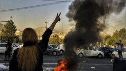  Eine Frau steht während einer Demonstration nach dem Tod der 22-jährigen Mahsa Amini vor einem brennenden Autoreifen und zeigt das Victory-Zeichen. Archivbild: 30.09.2022 