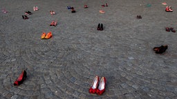 Auf einem PLatz stehen 44 Paare Damenschuhe, die mit roter Farbe befleckt sind. Teil einer Demonstration gegen Frauenmorde.