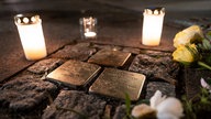 Kerzen und Blumen auf Stolpersteinen in Gedenken an Reichsprogromnacht. 