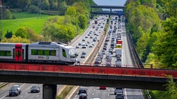 Eine S-Bahn fährt über die Brücke einer Autobahn, auf der viel Verkehr ist.