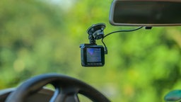 Eine Dashcam ist hinter der Windschutzscheibe installiert mit Blick ins Grüne außerhalbd es Autos.