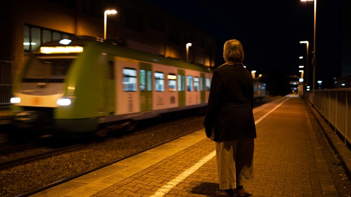 Eine Frau steht auf einem dunklen Bahngleis