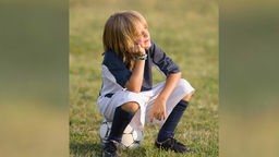 Symbolbild: Philosphie im Fußball – ein Junge sitzt auf einem Ball und blickt in den Himmel.