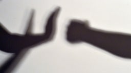 Der Schatten einer Faust trifft auf den Schatten zweier Hände die mit einer Geste Halt gebieten.
