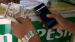 Ein Kunde tätigt eine mobile Geldüberweisung, bekannt als M-Pesa, an einem Safaricom-Vertreterstand, während er kenianische Schillinge in Nairobi, Kenia, hält.