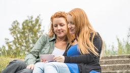 Zwei Frauen unterhalten sich, die eine zeigt der anderen ein Bild auf ihrem Smartphone