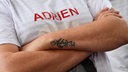 Auf den Arm eines Mannes ist der Name "Adrien" tätowiert