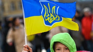 Ein Kind hält auf einer Demonstration eine ukrainische Fahne in die Höhe. 