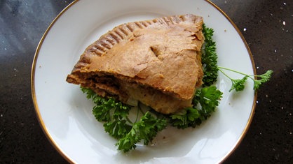 Überbackene Zwiebel-Käse-Pastete auf weißem Teller mit Petersilien-Deko.