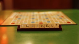 Auf einem Bänkchen des Spieleklassikers Scrabble liegen die Steine so angeordnet, dass sich das Wort "Freiheit" ergibt. Im Hintergrund ist unscharf das Spielbrett zu erkennen.