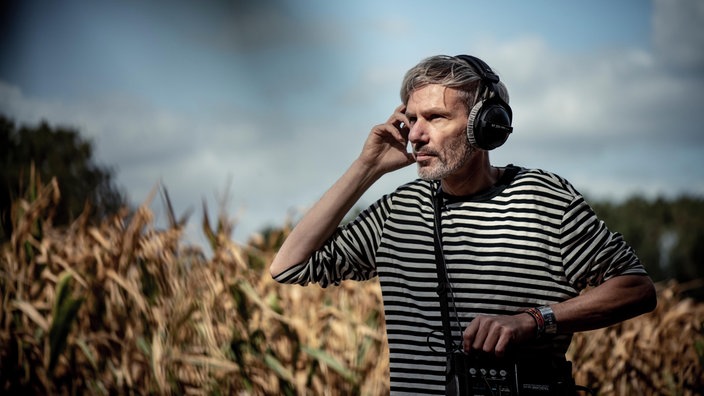 Kai Grehn, mit Kopfhörern und Tongerät, steht auf einem Feld