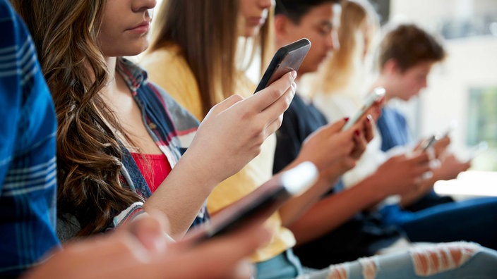 Schüler sitzen mit Smartphone in der Hand.