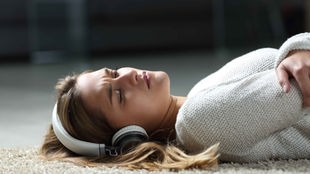 Symbolbild Jugendstudie: Eine Frau liegt auf dem Boden und hört Musik mit einem Kopfhörer