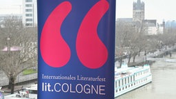 Logo und Schriftzug der 24. Lit.Cologne, Im Hintergrund ist der Rhein und ein Teil der Kölner Altstadt zu sehen. 