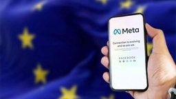 Eine Händ hält ein Smartphone mit Meta-App, im Hitergrund weht eine Flagge der Europäischen Union. 