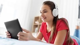 Mädchen mit Kopfhörern, das Musik auf einem Tablet-PC hört.